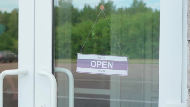 Ein Mann wechselt ein Schild mit der Aufschrift OPEN gegen ein Schild mit der Aufschrift GESCHLOSSEN während der COVID-19-Pandemie. Infotafel an einer transparenten Tür oder in einem Schaufenster — Stockvideo