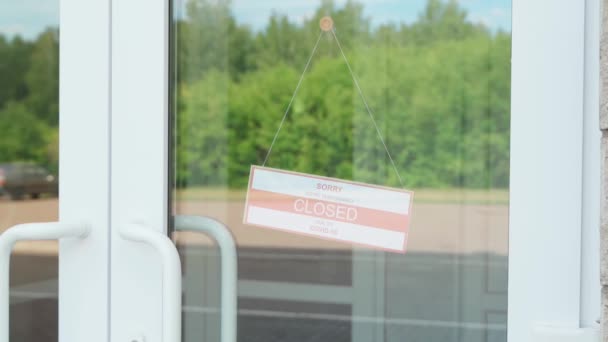 Un homme enlève un panneau qui lisait FERMÉ pendant la pandémie de COVID-19 qui pendait à une porte transparente ou dans une devanture — Video