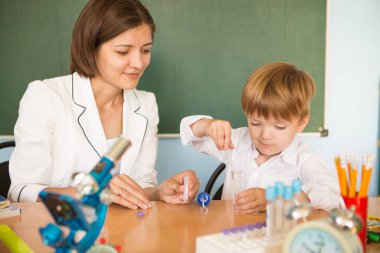 Öğretmen küçük çocuğa yazı dersinde yardım ediyor. Okul konseptine dönelim.