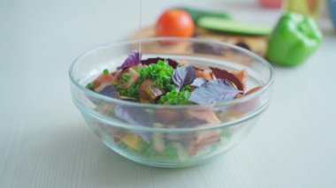 Bir kase sebze salatasına zeytin yağı dökülüyor.