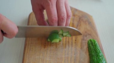 Erkek eli kesme tahtasındaki salatalığı kesiyor.