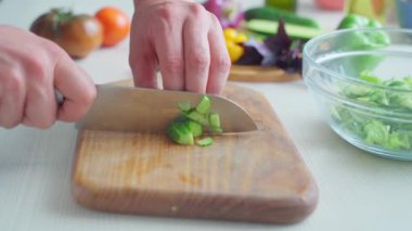 Erkek eli kesme tahtasındaki salatalığı kesiyor.