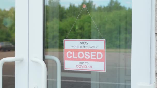 Bir adam COVID-19 salgını sırasında saydam bir kapıda ya da vitrinde asılı olan "Kapalı" tabelasını kaldırır. — Stok video
