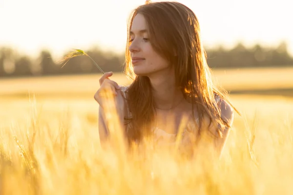 Meisje in een jurk in een tarweveld bij zonsondergang — Stockfoto