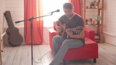 Adam gitar çalıyor ve mikrofonla şarkı söylüyor.