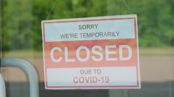 Ein Mann entfernt ein Schild mit der Aufschrift GESCHLOSSEN während der COVID-19-Pandemie, das an einer transparenten Tür oder in einem Schaufenster hing — Stockvideo
