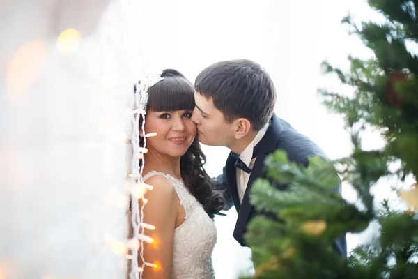Pasgetrouwden kussen in de buurt van een kerstboom. — Stockfoto