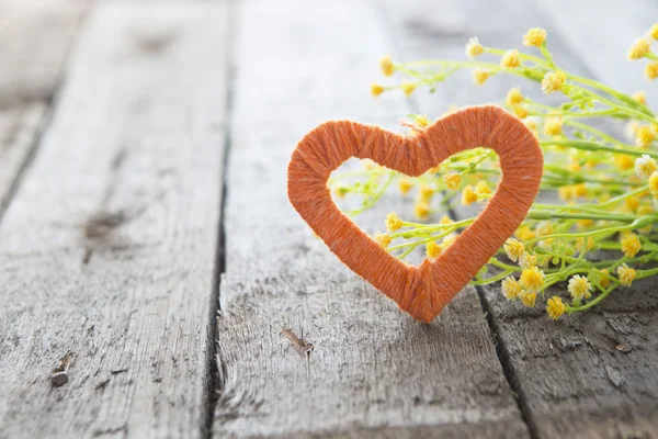 Coeur et fleurs sauvages jaunes sur une vieille table en bois . — Photo