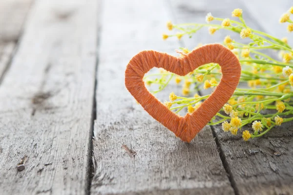Hjärta och gula blommor på ett gammalt träbord. — Stockfoto