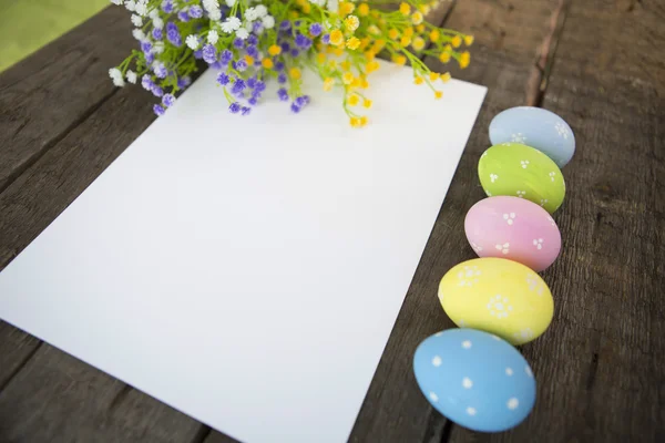 Pasen-wenskaart met eieren en wilde bloemen boven hout. — Stockfoto