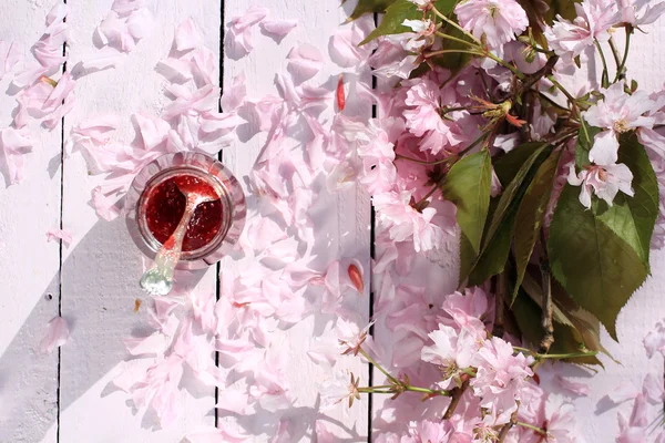 Un pot de confiture de framboises fraîches sur une table rustique couverte de fleurs de cerisier, fond de petit déjeuner romantique, gros plan, dans le jardin — Photo
