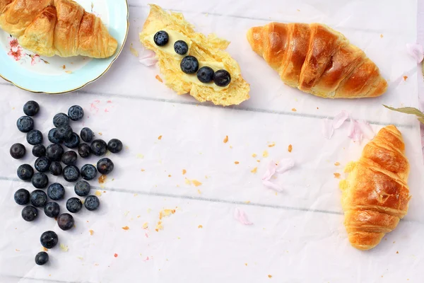 Deliziosa colazione con croissant freschi e bacche mature su vecchio sfondo di legno, focus selettivo — Foto Stock