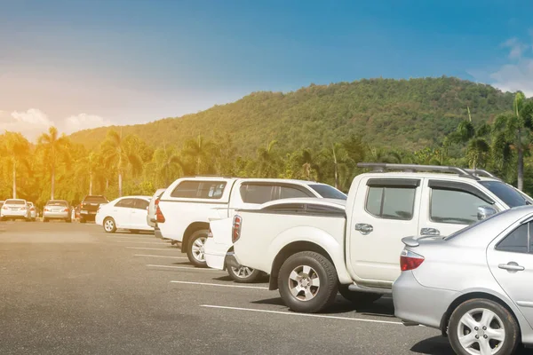 Car parked in large asphalt parking lot with trees, blue sky and mountain background. Outdoor parking lot with nature and green environment of travel transportation concep