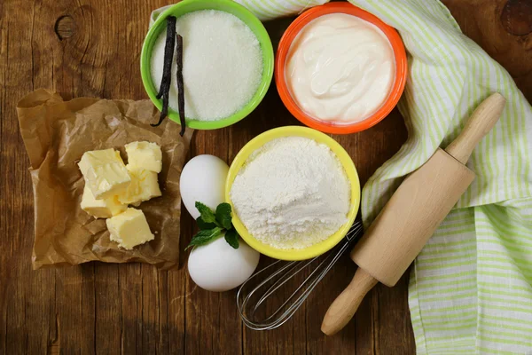 Ingrediënten voor gebak - boter, melk, eieren, bloem en vanille suiker op een houten achtergrond — Stockfoto