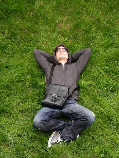Young man in casual clothes resting on the green grass — Stock Photo, Image