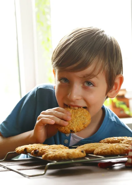 Blond boy eating oatmeal cookies on kitchen — Stock Photo, Image