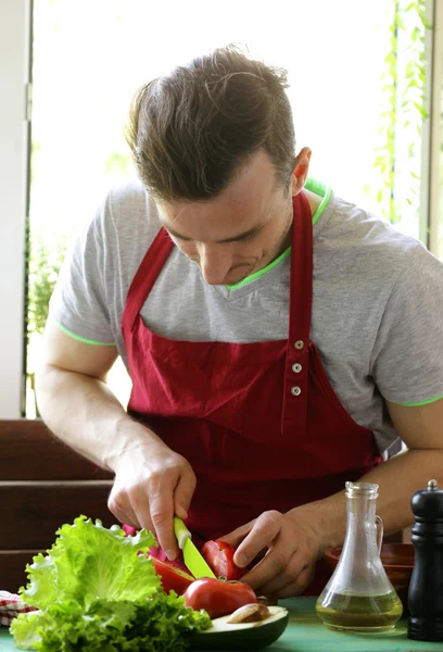 Homem cozinhar salada de legumes (tomates, alface, pepinos) em uma tábua de madeira — Fotografia de Stock