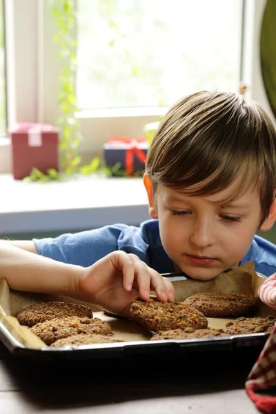 Blond boy eating oatmeal cookies on kitchen — Stock Photo, Image