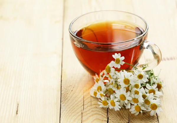 Glass cup with tea and chamomile on a wooden background — Stock Photo, Image