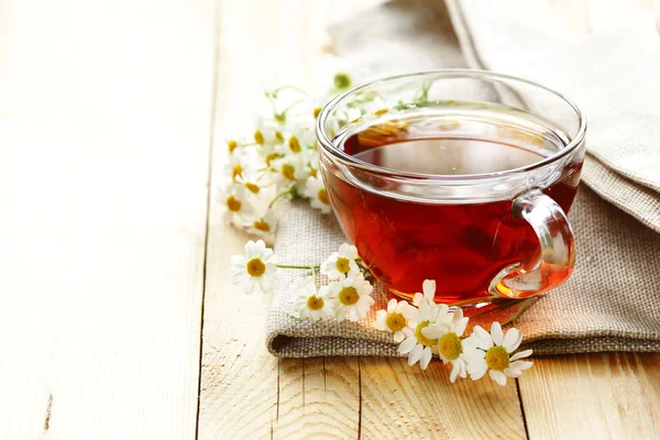Glass cup with tea and chamomile on a wooden background — Stock Photo, Image