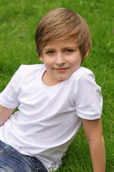 Mignon garçon blond est couché sur l'herbe verte dans le parc — Photo