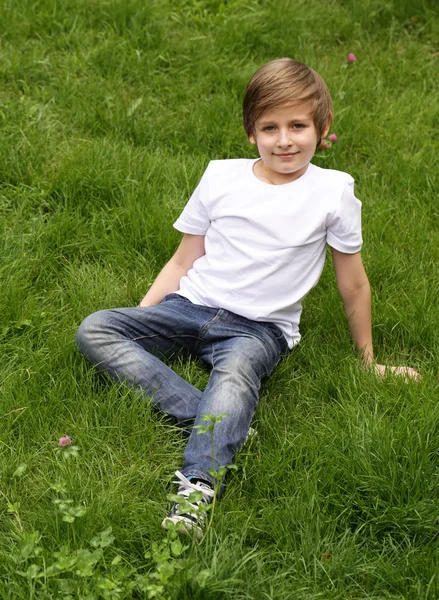 Netter blonder Junge liegt auf grünem Gras im Park — Stockfoto