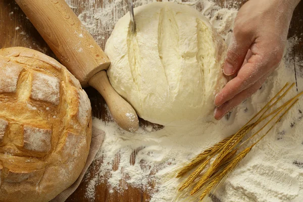 Chef hands with dough and homemade natural organic bread and flour on a wooden background