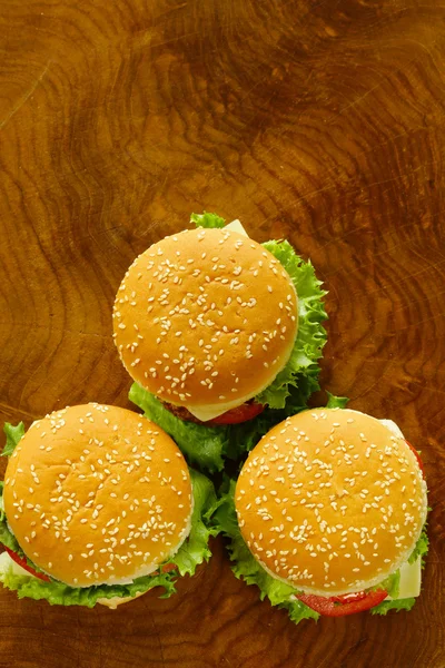 Cheeseburger s zeleným salátem a rajčaty na dřevěné pozadí, pohled shora — Stock fotografie