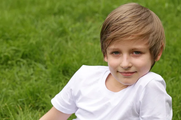 귀여운 금발 소년 공원에서 푸른 잔디에 앉아 — 스톡 사진