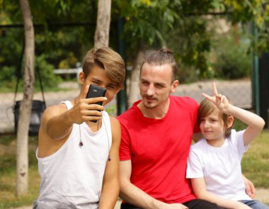 Baba ve iki oğlu bir bankta oturan ve smartphones vasıl bak
