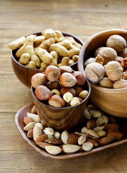 Different kinds of nuts (almonds, walnuts, hazelnuts, peanuts) in a bowl on a wooden table — Stock Photo, Image