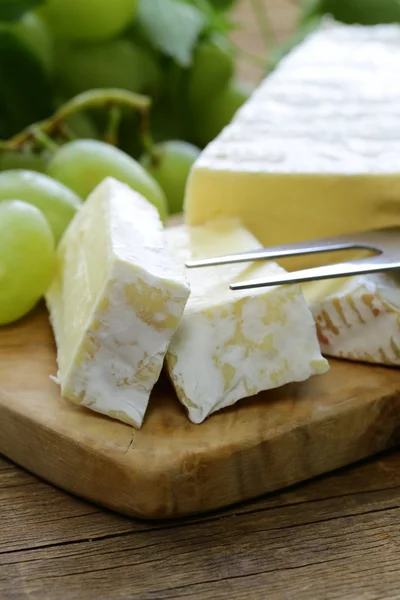 Queso brie suave con uvas dulces en una tabla de madera —  Fotos de Stock