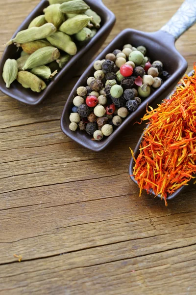 Spices (saffron, pepper and cardamom) in the scoop on a wooden table — Stock Photo, Image