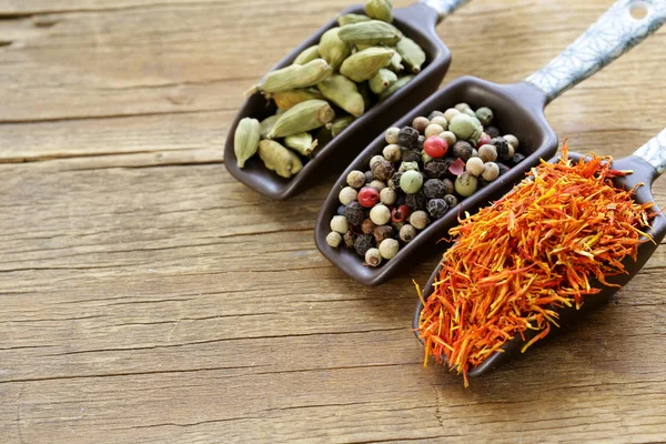 Spices (saffron, pepper and cardamom) in the scoop on a wooden table — Stock Photo, Image