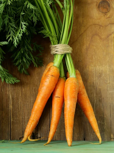 Fresh organic carrots with green leaves on a wooden background — Stock Photo, Image