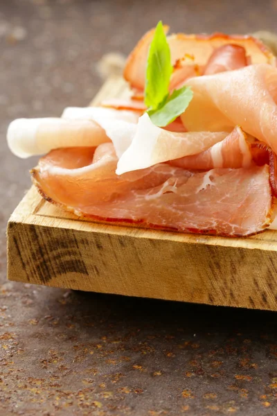 Rökt skinka jamon (Parma) med basilikablad på en planka — Stockfoto