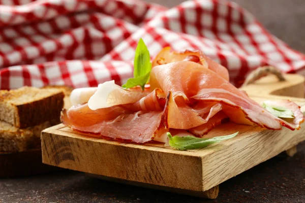 Rökt skinka jamon (Parma) med basilikablad på en planka — Stockfoto