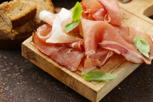 Rökt skinka jamon (Parma) med basilikablad på en planka — Stockfoto