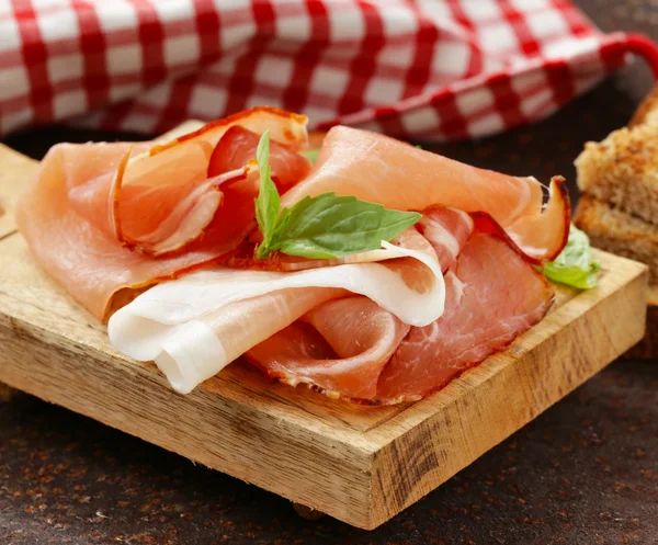 Rökt skinka jamon (Parma) med basilikablad på en planka — Stockfoto