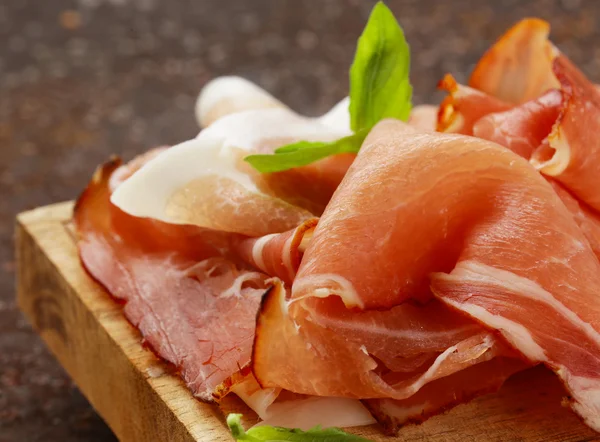 Jambon de jambon fumé (Parme) avec feuilles de basilic sur une planche de bois — Photo