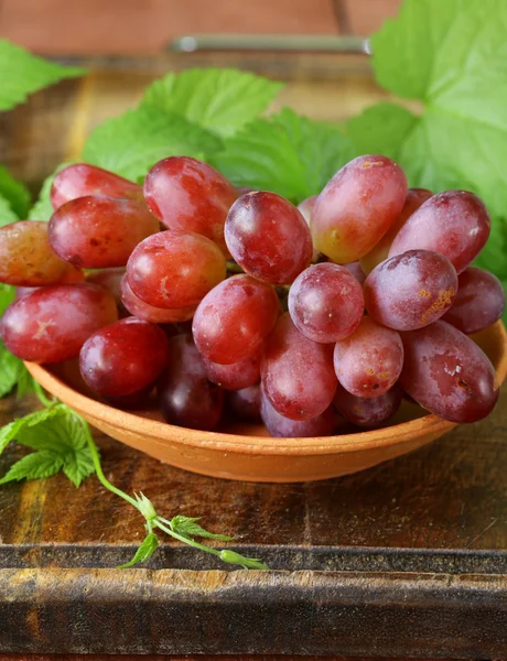 Ветвь красного спелого винограда с зелеными листьями на деревянном столе — стоковое фото