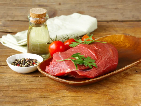 Carne fresca de res cruda con pimienta y hierbas en un plato de madera — Foto de Stock