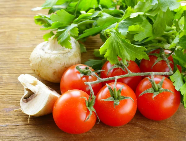 Mix vegetables (tomatoes, cucumbers, mushrooms, herbs) on a wooden table — Stock Photo, Image