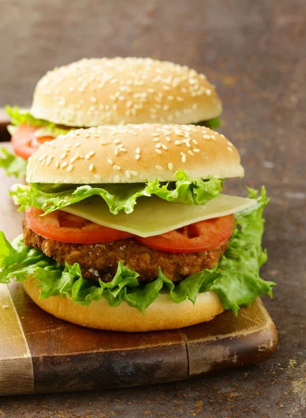 Tradiční cheeseburger s zeleným salátem a rajčaty na dřevěné pozadí — Stock fotografie