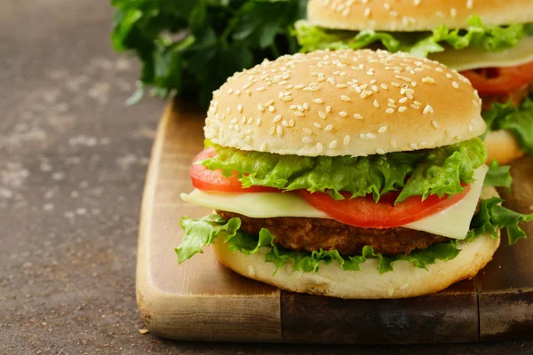 Tradiční cheeseburger s zeleným salátem a rajčaty na dřevěné pozadí — Stock fotografie