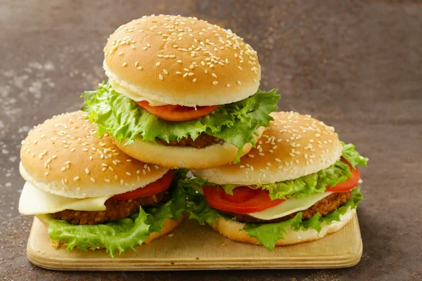 Tradiční cheeseburger s zeleným salátem a rajčaty na dřevěné pozadí — Stock fotografie
