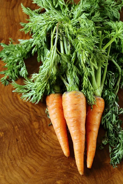 Ripe organic carrots with green leaves on a wooden background — Stock Photo, Image