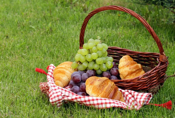 Cesta de piquenique com croissants e uvas em uma grama verde — Fotografia de Stock