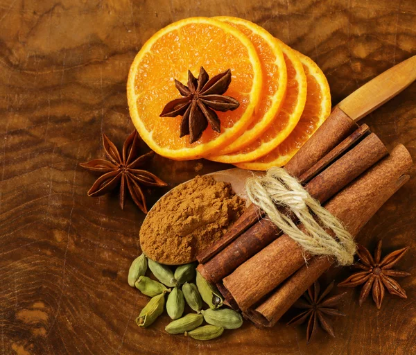 Fragrant cinnamon sticks, star anise, cardamom and orange on a wooden background — Stock Photo, Image