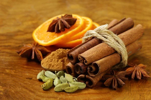 Fragrant cinnamon sticks, star anise, cardamom and orange on a wooden background — Stock Photo, Image